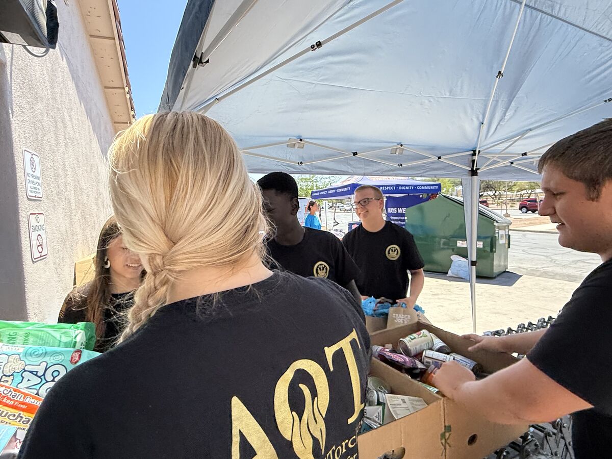 AOT volunteers smiling while sorting canned goods under the canopy tent