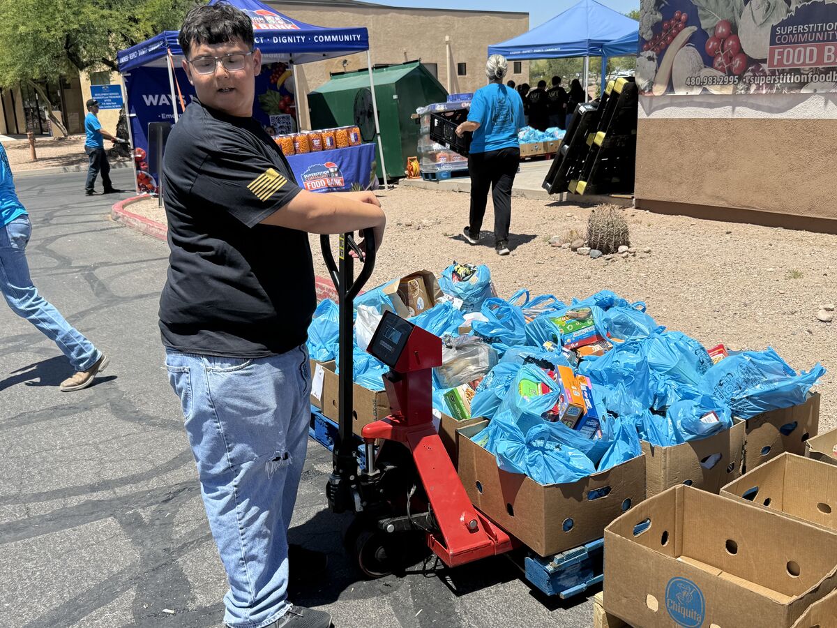 Young AOT volunteer operating a pallet jack loaded with blue bags of food donations
