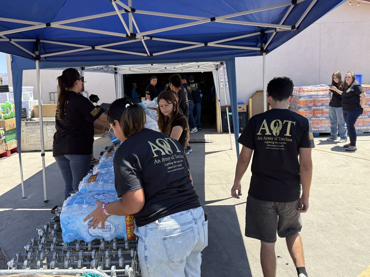 AOT volunteers carrying water and supplies under blue tents at the food drive event
